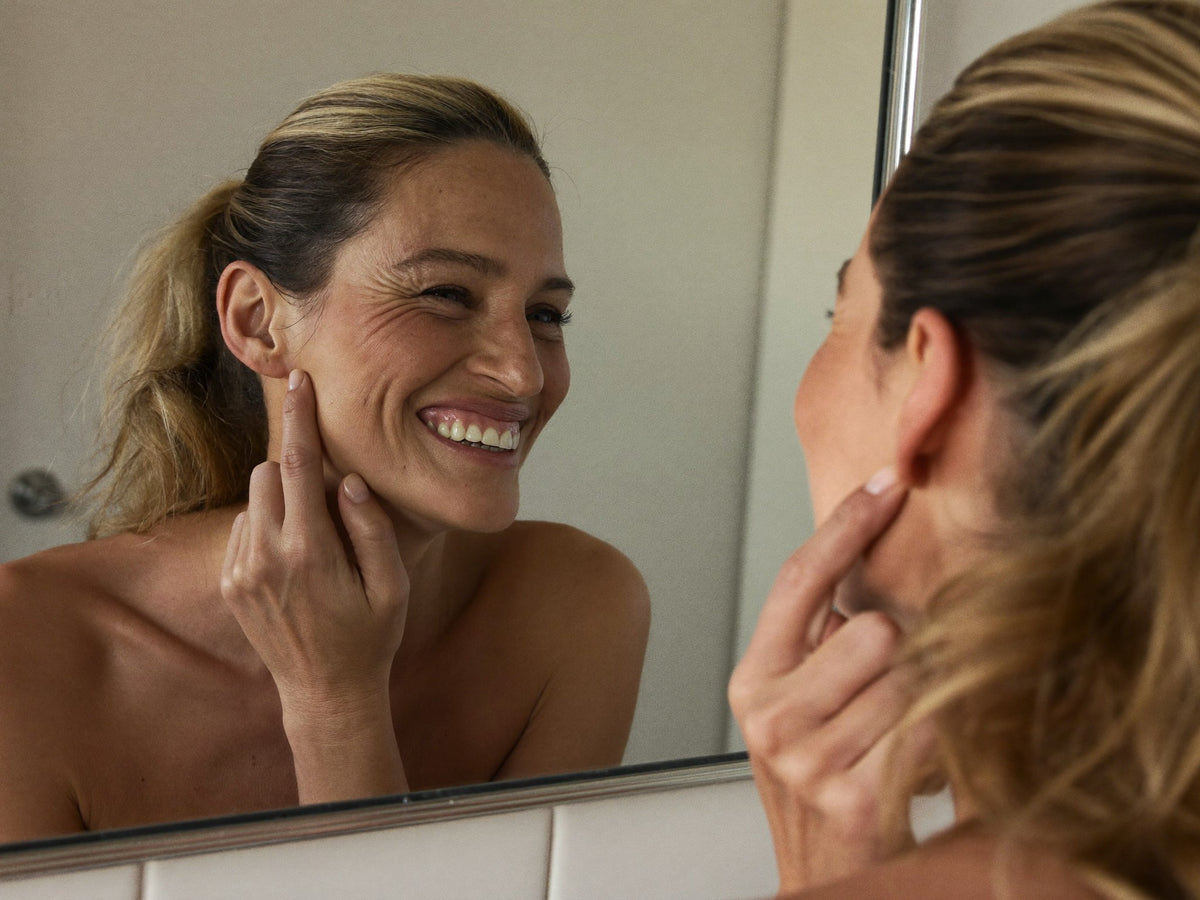 Femme souriante qui se regarde dans le miroir de sa salle de bains, le matin